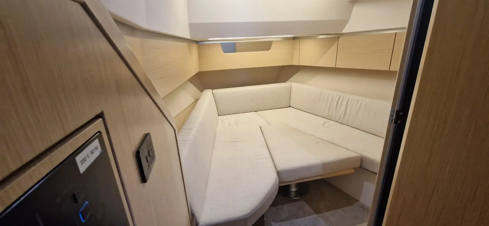 Interior of a modern boat cabin with a compact seating area, light wood finishes, and a view of a power socket.